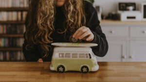 This is an image of a woman placing money in a piggybank because the cost of living is so high in the UK.